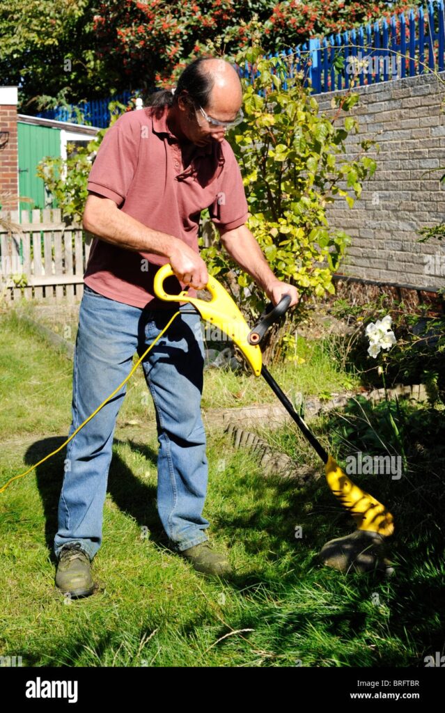 Man Using An Electric Grass Cutting Tool To Cut Long Grass In His Garden Stock Photo Alamy